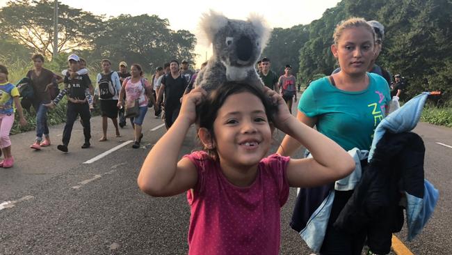 a young member of the caravan carries a stuffed koala, seemingly unaware of the perils that may lie ahead.