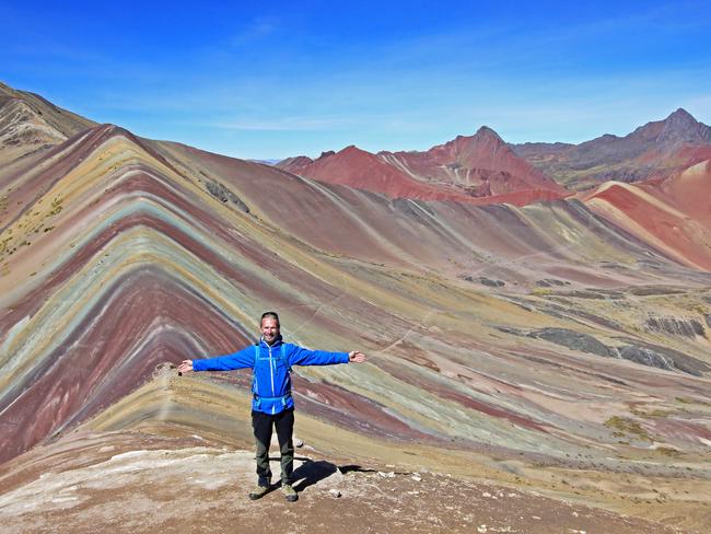 The photographer posing in front of the beautiful colored Rainbow Mountain panorama near Cusco Peru. Nice view into the hole valley. Located about 20km south of Ausangate mountain.