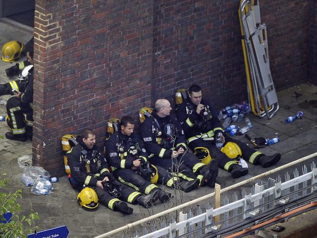 Firefighters rest after battling the blaze all night. Restricted access meant many were forced to run carrying heavy equipment. Picture: AP Photo/Matt Dunham.