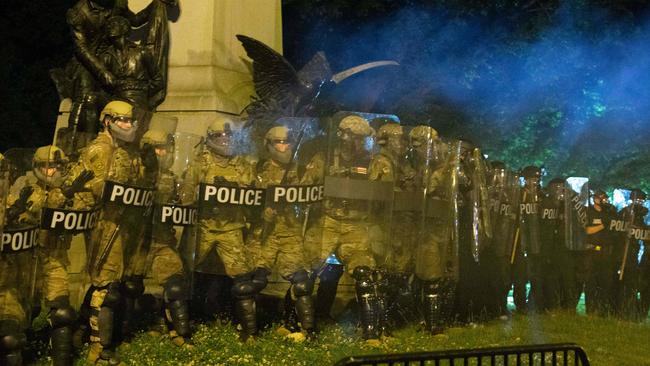 Police officers in riot gear watch demonstrators as they chant outside of the White House.