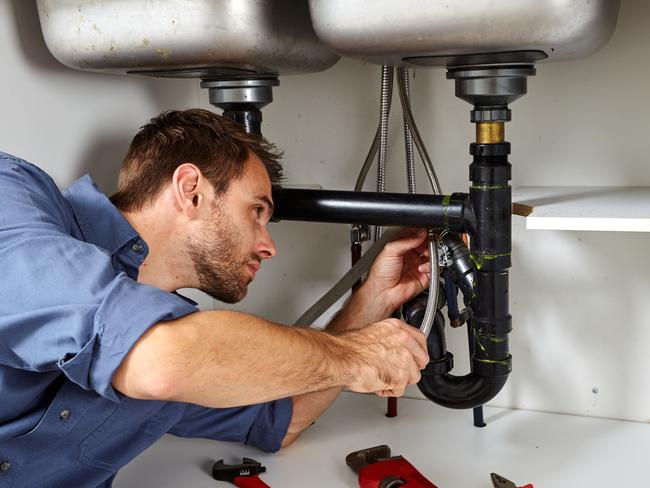 TRADESMAN:  Plumber with tools doing reparation in the kitchen.