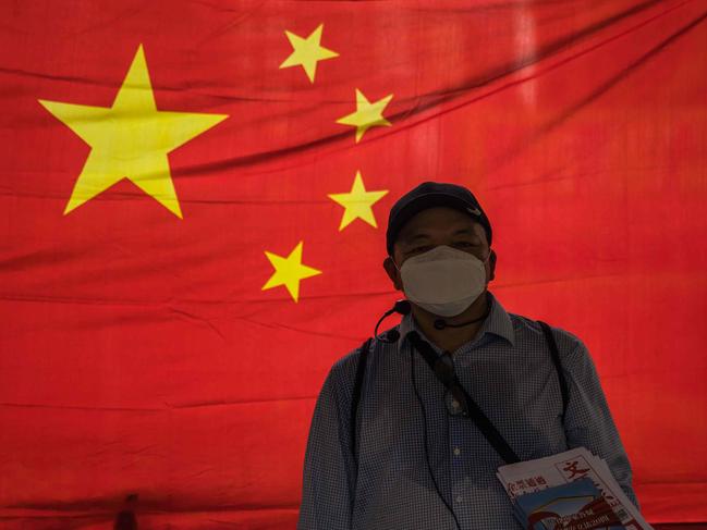 A pro-government supporter hands out newspapers in front of a Chinese national flag in Hong Kong on July 1, 2020, on the 23rd anniversary of the city's handover from Britain to China. - Hong Kong marks the 23rd anniversary of its handover to China on July 1 under the glare of a new national security law imposed by Beijing, with protests banned and the city's cherished freedoms looking increasingly fragile. (Photo by DALE DE LA REY / AFP)