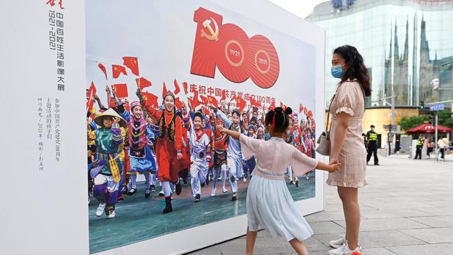 A woman and child visi an outdoor photography exhibition promoting the 100th anniversary of the founding of the Communist Party of China along a business street in Beijing. Picture: AFP