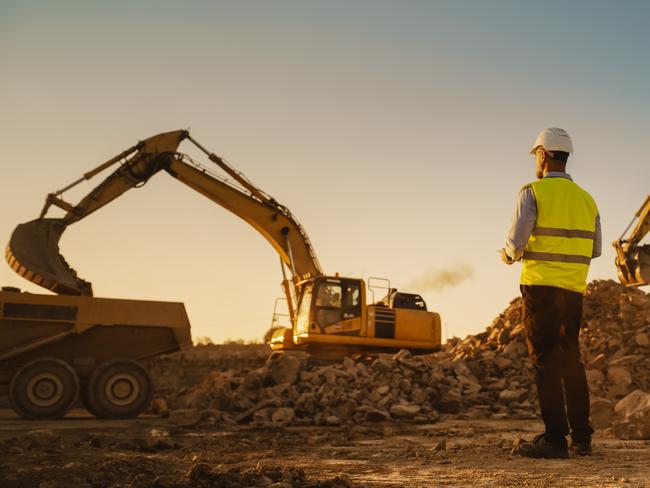 Man Inspecting Building Progress. Excavator Loading Materials Into Industrial Truck