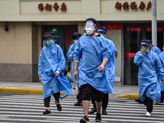 Workers wearing protective gear cross a street during a Covid-19 coronavirus lockdown in the Jing'an district of Shanghai. Picture: AFP