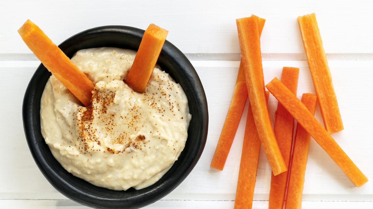 Hummus with carrot sticks. Top view over white timber.