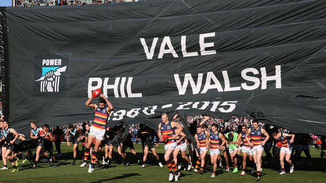 Adelaide and Port Adelaide players run through the same banner to honour Phil Walsh in 2015. Picture: AAP Image/Ben Macmahon