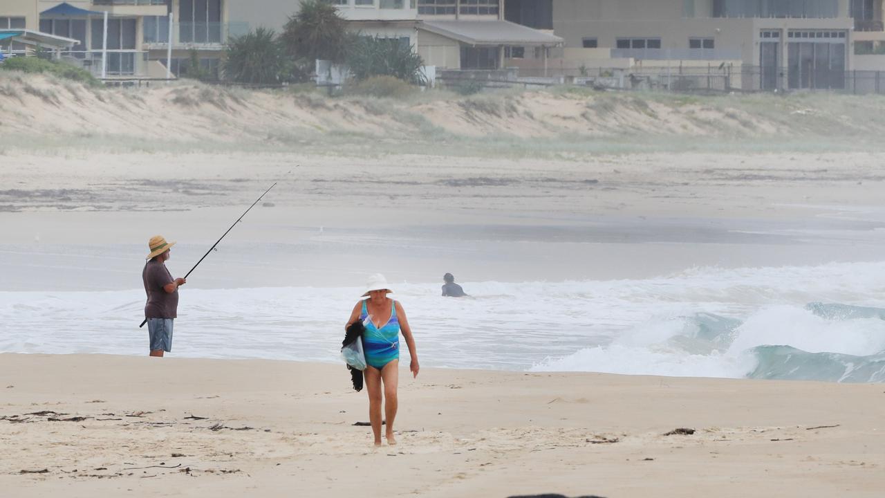 A fisherman and walker brave conditions at Palm Beach this morning as wet weather descended over the Gold Coast. Photo: Scott PowickNEWSCORP