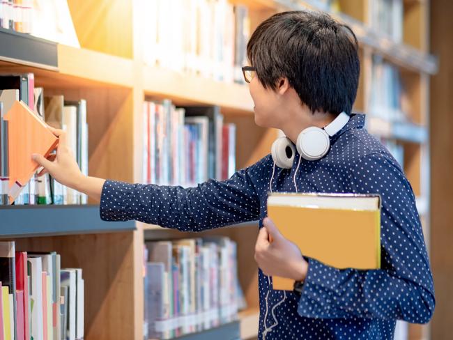 Generic image of a man picking books from a shelf at a library.