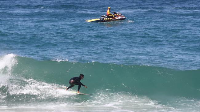 A surfer rides a wave at Burleigh as a lifesaver patrols on a jet ski. Picture: Jason O'Brien