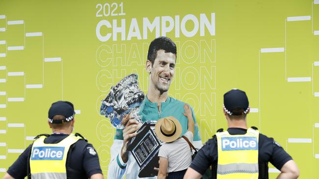 A spectator touches a banner of 2021 Men's Australian Open winner Novak Djokovic as police officers look on during day one of the 2022 Australian Open at Melbourne Park.