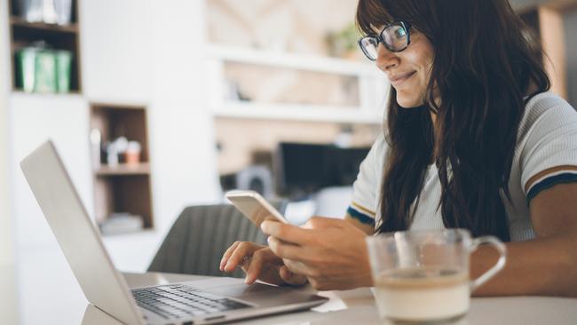 Young woman enjoying home office using laptop and smartphone