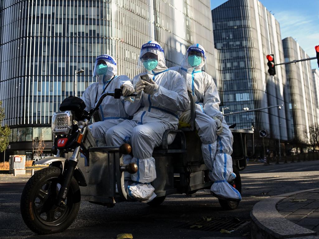 Workers wearing personal protective equipment (PPE) ride on a tricycle along a street in Beijing. Picture: AFP.