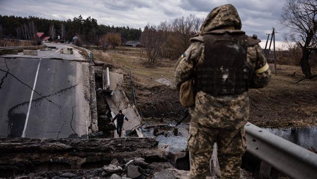 An Ukrainian serviceman watches a civilian crossing a blown up bridge in a village east of Brovary on March 6, 2022. Picture: Dimitar Dilkoff/AFP