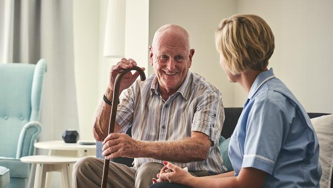 Smiling retired senior man sitting on sofa with female home carer at care home