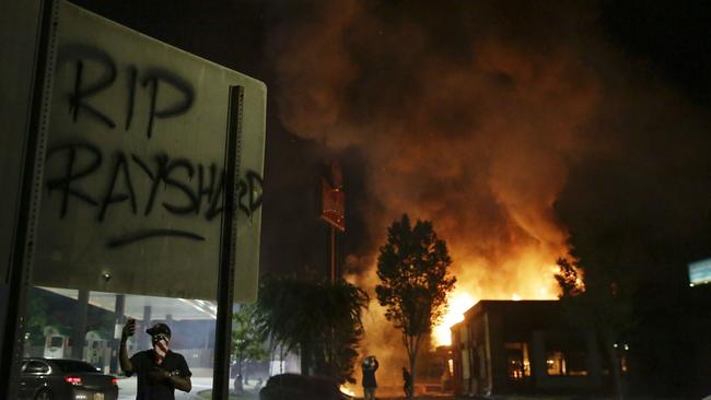 "RIP Rayshard" is spray painted on a sign as as flames engulf a Wendy's restaurant where Rayshard Brooks was shot and killed by police.