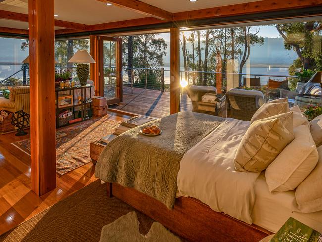 Huon River Hideaway’s bedroom features picturesque views from its expansive floor-to-ceiling windows, a generous comfy bed, as well as gleaming Tasmanian oak floors and celery top pine pillars. Picture: Jon Jarvela Photography