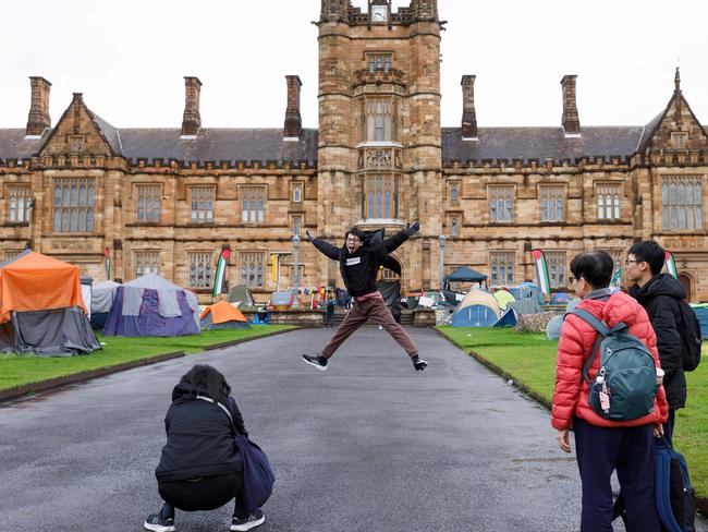 SYDNEY, AUSTRALIA - NewsWire Photos JUNE 15 2024. International students pose for pictures with the historic sandstone buildings of Sydney Uni, which are surrounded by a pro-gaza & Palestine tent camp. The uni has ordered the pro-Palestinian encampment to pack up and leave campus eight weeks after the tent protest appeared on its lawns. Picture: NewsWire / Max Mason-Hubers