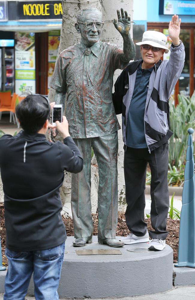 A tourist poses for a photo alongside a statue of Sir Bruce Small on the corner of Elkhorn and Cavill Ave in Surfers Paradise. Picture: Glenn Hampson.