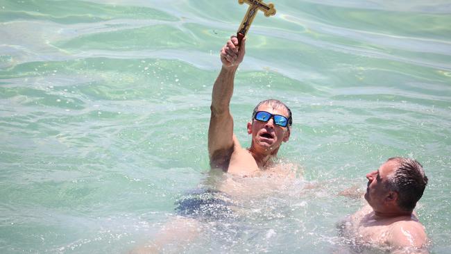A‘Victor’ holds up the cross after snatching it from the water. Picture: Russell Millard