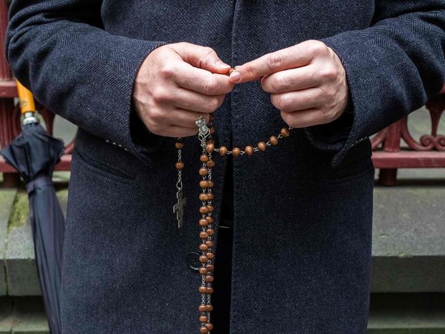 A supporter of Australian Cardinal George Pell prays while holding rosary beads outside the Supreme court of Victoria in Melbourne on June 5, 2019. - Pell left his prison cell to attend the opening hearing in his appeal against the conviction for children sexual abuse. (Photo by ASANKA BRENDON RATNAYAKE / AFP)