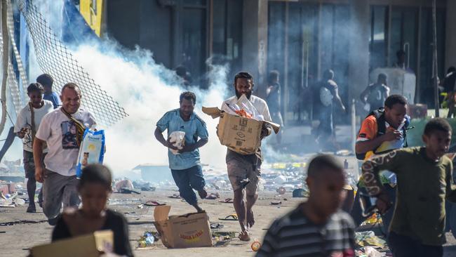 People run with merchandise as crowds leave shops with looted goods amid a state of unrest in Port Moresby on Wednesday. Picture: AFP