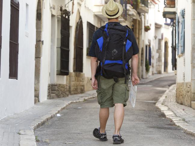 Man walking with backpack and map lost in town - from behind