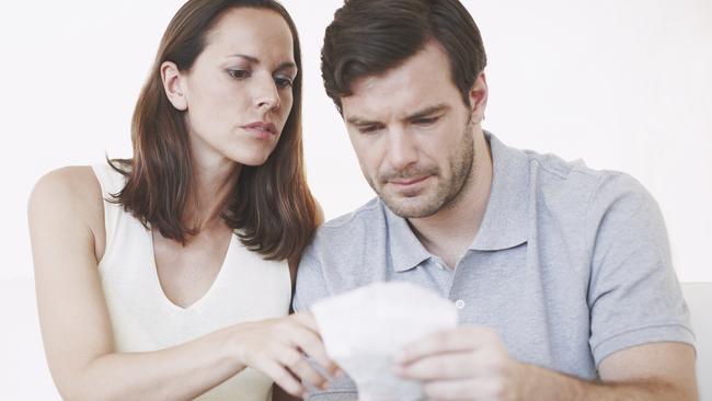 A married couple looking slightly concerned as they inspect bills and discuss their home finances