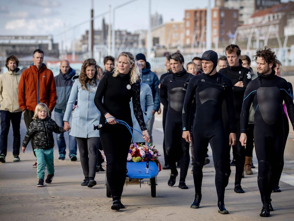 Mourners carry a floral tribute on a surfboard as they arrive at a commemoration at The Shore Surf Club at Scheveningen.