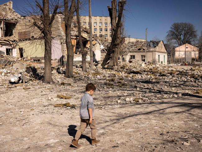 A child walks in front of a damaged school in the city of Zhytomyr, northern Ukraine, on March 23, 2022. (Photo by FADEL SENNA / AFP)