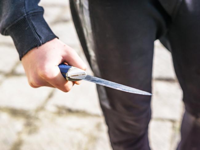 Close-up of a young man's hand with a knife, a big blade. Arrogance and violence among young people. Shallow depth of focus.