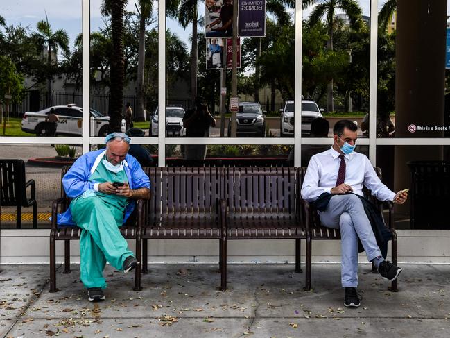 A doctor (left) wearing personal protective equipment (PPE) uses his mobile phone as he sits outside Jackson Memorial Hospital in Miami. Picture: AFP