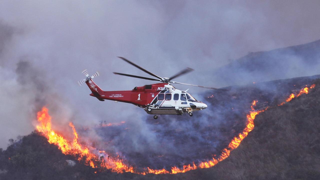 A helicopter flies over homes threatened by the wind-driven fire in Pacific Palisades. Picture: AFP