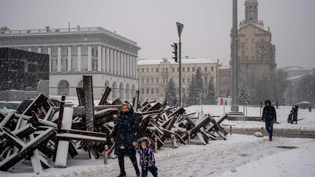 A woman and child walk past antitank steel hedgehogs covered with snow along Independence Square in the Ukrainian capital Kyiv. Picture: AFP