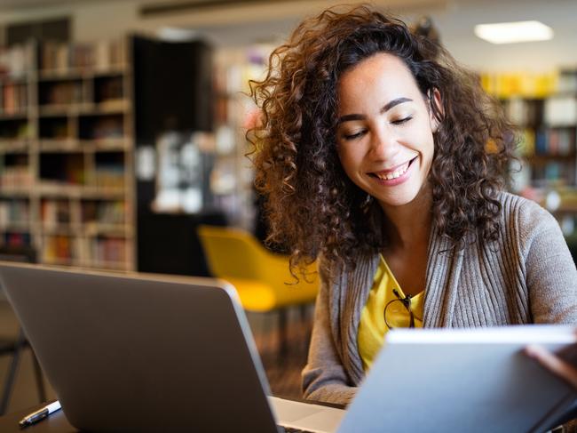 Young afro american woman sitting at table with books and laptop for finding information. Young student taking notes from laptop and books for her study in library.