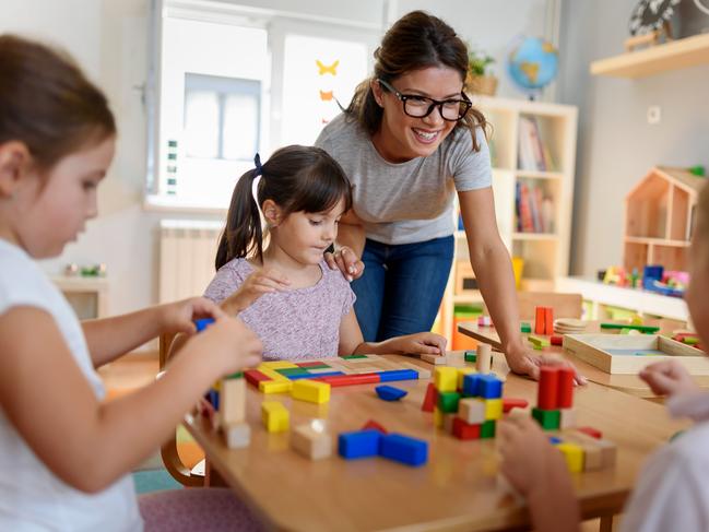 Preschool teacher with children playing with colorful wooden didactic toys at kindergarten