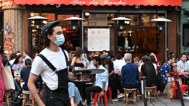 A waiter wearing a face mask serves clients while people eat and have drinks on the terrace of the cafe-restaurant Le Bar du Marche in Paris. Picture: AFP