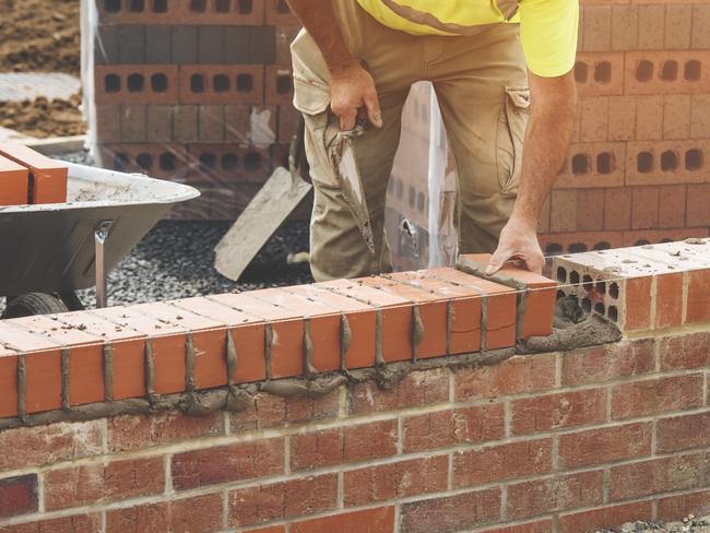 Developing Queensland - Industrial bricklayer laying bricks on cement mix on construction site.