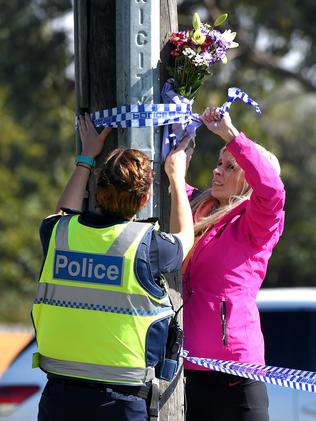 A police officer helps a woman lay some flowers at the scene. Picture: Nicole Garmston