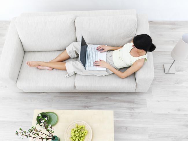 Full length of a young lady sitting on sofa, working on laptop