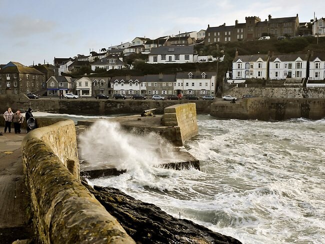 People walk along a path as waves crash onto a seawall protecting the harbor of Porthleven, Cornwall, southwest England.