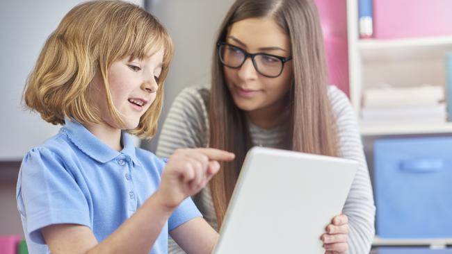 a young teacher listens as her young pupil explains what she is reading on a digital tablet . The little girl is excited as she explains to her teacher . Picture: Istock