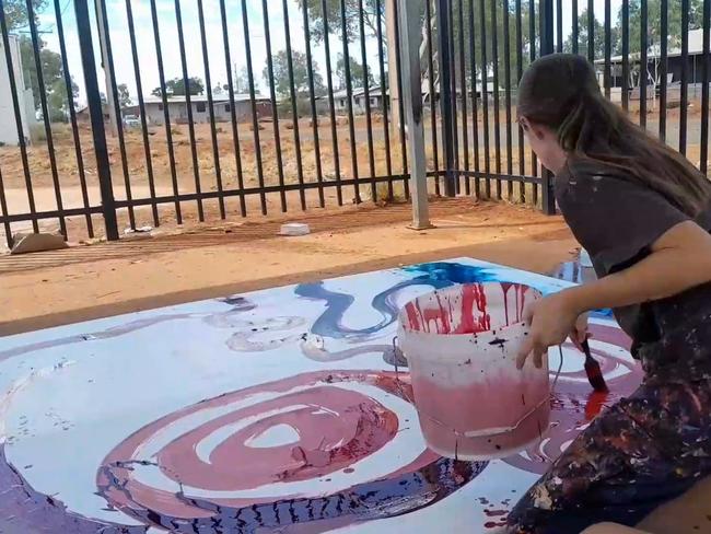 Stills taken from video where a non-indigenous employee is seen contributing to a painting by (Indigenous) artist Yaritji Young. The employee wearing darker clothing and holding a paint brush is Rosie Palmer, manager of Tjala Art in the settlement of Amata in the APY Lands.