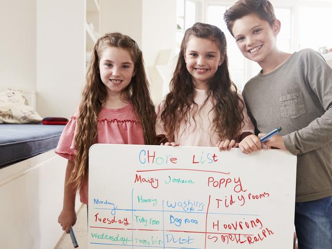 Portrait Of Children Making List Of Chores On Whiteboard At Home