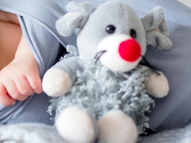 Little newborn baby boy, looking curiously at camera, lay dawn in bed, holding little toy