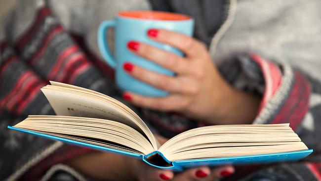 woman reading a book and holding a mug of hot beverage