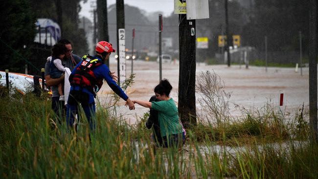 A rescue worker helps residents cross a flooded road during heavy rain in western Sydney on March 20, 2021, amid mass evacuations being ordered in low-lying areas along Australia's east coast as torrential rains caused potentially "life-threatening" floods across a region already soaked by an unusually wet summer. (Photo by Saeed KHAN / AFP)