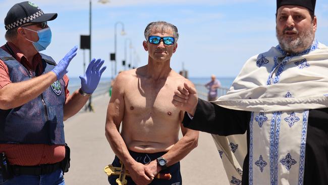 ‘Victor’, clutching the cross, after being questioned by police. Father Michael Psaromatis addresses the booing crowd. Picture: Russell Millard
