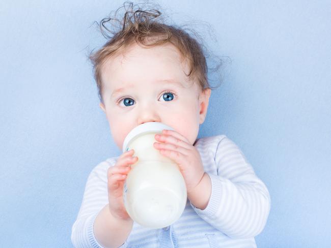 Sweet little baby with beautiful blue eyes drinking milk in a plastic bottle relaxing on a blue knitted blanket