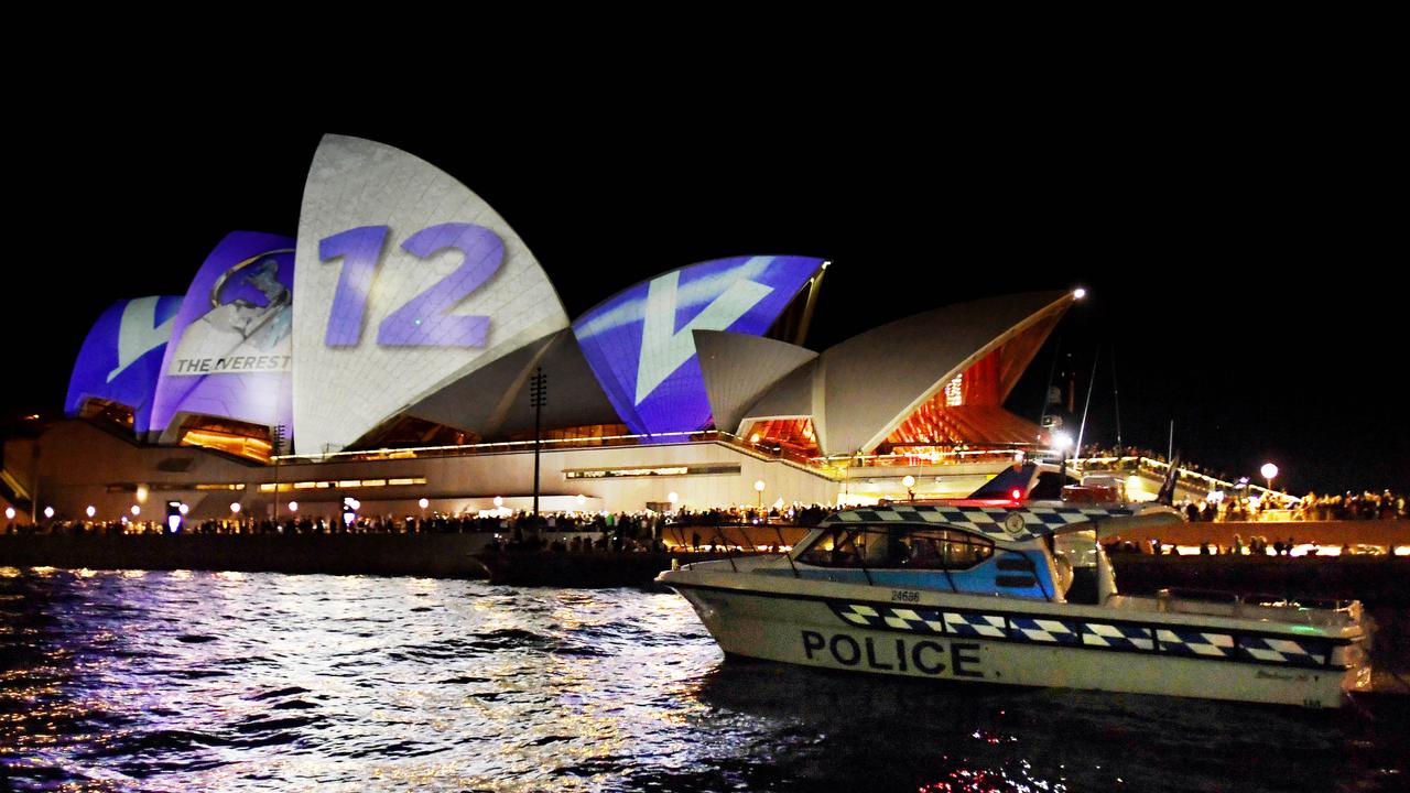 The Sydney Opera House is lit up with spots of light as protesters gather at the base of it and police go by. Picture: Tracey Nearmy